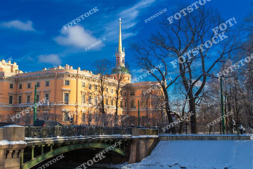 Фотография зимнего Санкт-Петербурга с видом на инженерный шлюз и историческую архитектуру города. Улицы покрыты снежным покрывалом, создавая сказочную атмосферу северной столицы. На снимке видны старинные здания и музеи, подчеркивающие культурное наследие Петербурга, а зимний свет и отражения на воде добавляют кадру глубины и художественной выразительности. Фотография отлично передает холодное очарование города, его архитектурную гармонию и богатую историю, делая изображение идеальным для туристических публикаций, коллекций фотографий, оформления интерьеров или постеров с зимним Петербургом.